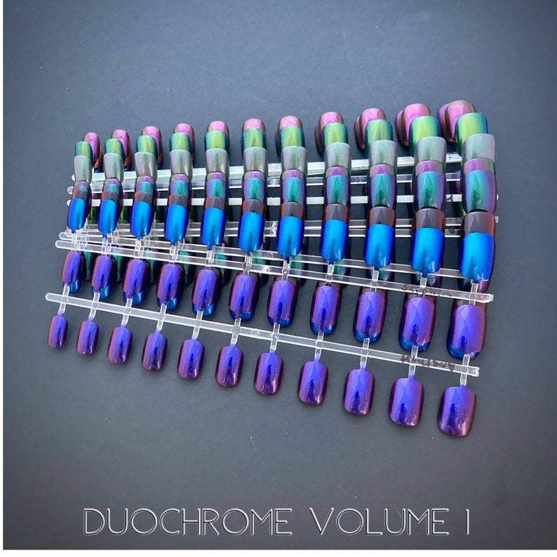A bundle of short duochrome nails in purple, blue, green and maroon on top of a black background. White text bottom center reads Duochrome Volume 1.