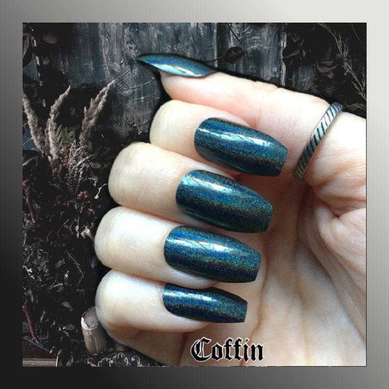White female hand wearing black holographic coffin nails shown on a black textured background. Text center bottom reads coffin
