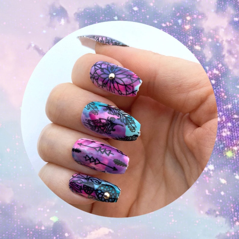 female had wearing purple and blue coffin style press on nails. press on nails have flower designs and a small crystal in the center of the design