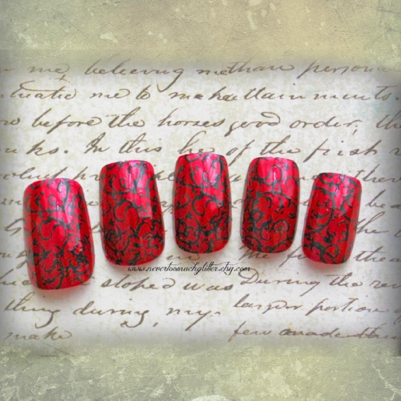 5 red square false fingernails with black geometric detailing rest on a beige paper with old fashioned script. There is a textured beige frame around the image.