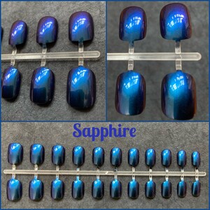 Short blue purple duochrome false nails shown on a black background. Top two photos show close up view. Text reads sapphire. bottom picture shows full set of 24 press on nails.