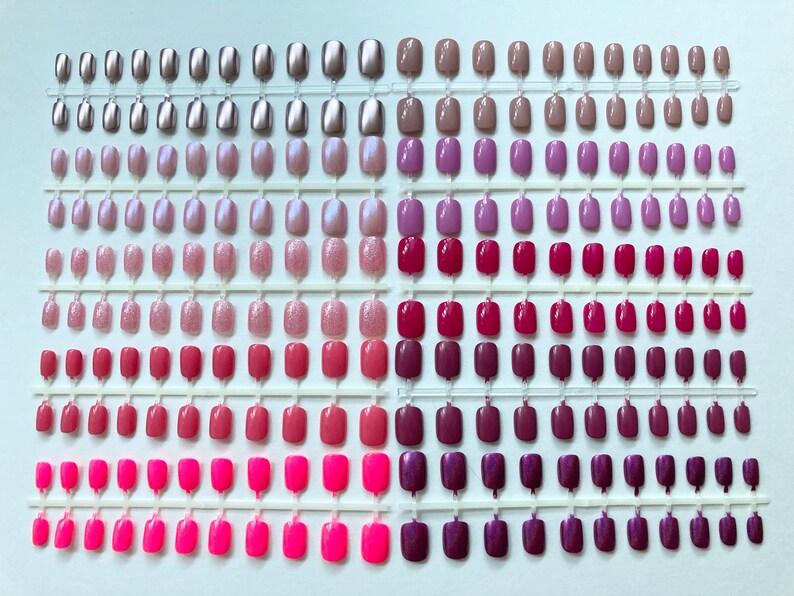 10 sets of short oval press on nails are displated. Magenta, bubblegum pink, pink glitter, neutral pink, neon, iridescent pink shell, fuchsia, metallic pink and medium pink nails are placed on a white background.