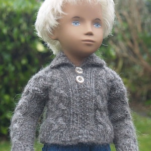 May include: A doll with blonde hair wearing a grey knitted sweater with two buttons and blue jeans.