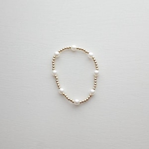 May include: A delicate gold bracelet with small white pearls. The bracelet is made of tiny gold beads and features a simple design.