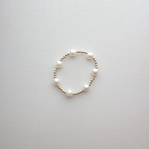 May include: A gold bracelet with white pearl beads.