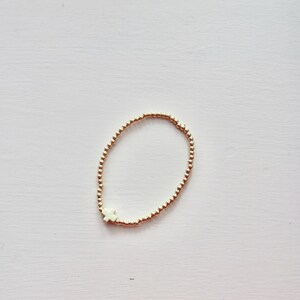 May include: A gold beaded bracelet with a white cross charm.