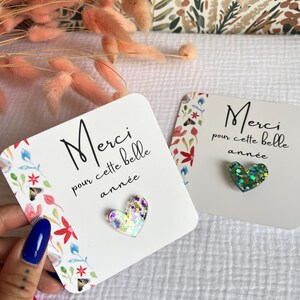 May include: Two white cards with floral designs and the text "Merci pour cette belle ann&eacute;e" (Thank you for this beautiful year) with a glittery heart on each card. The heart on the left card is iridescent and the heart on the right card is green.
