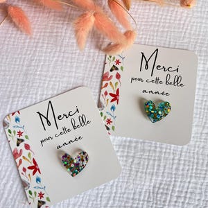 May include: Two white cards with floral designs and the text "Merci pour cette belle ann&eacute;e" in black. Each card has a heart-shaped glitter embellishment.