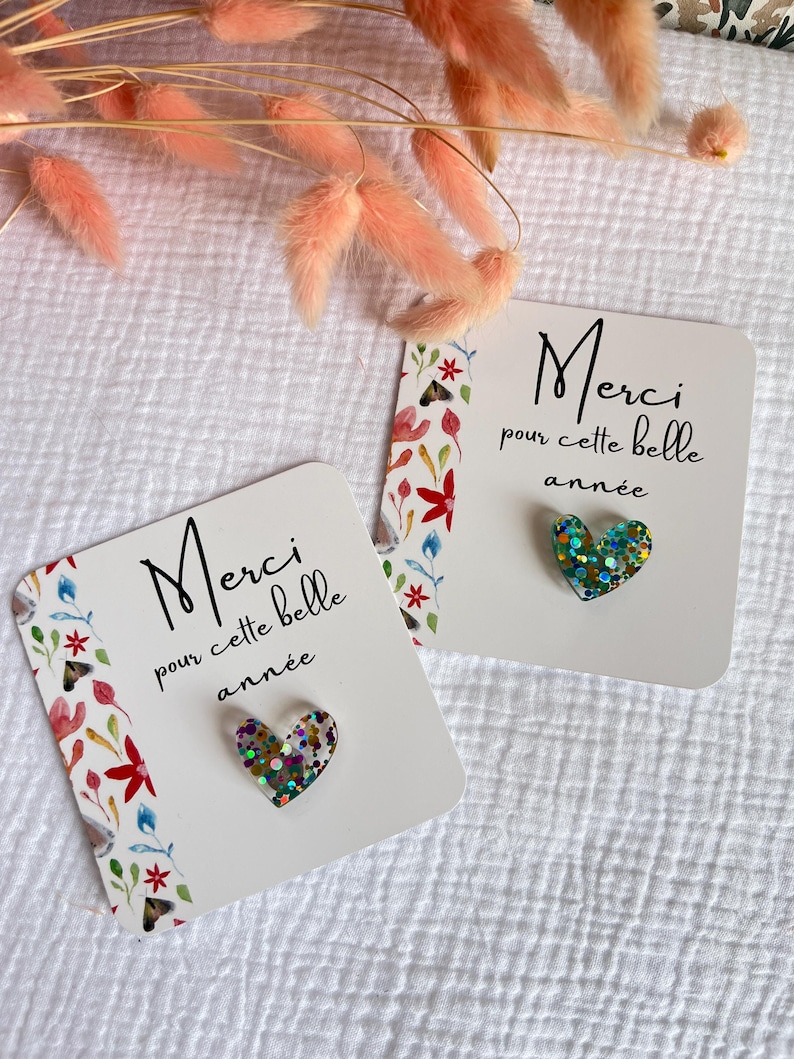 May include: Two white cards with floral designs and the text "Merci pour cette belle ann&eacute;e" in black. Each card has a heart-shaped glitter embellishment.