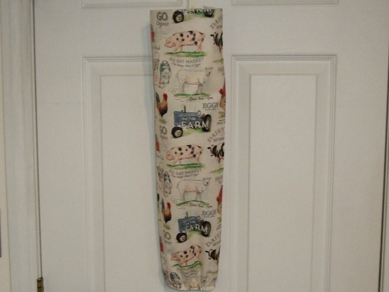 K&ouml;nnte beinhalten: Ein wei&szlig;er Plastik-Taschenspender mit einem Bauernhof-Motiv. Der Spender zeigt ein sich wiederholendes Muster aus Schweinen, K&uuml;hen, H&uuml;hnern und einem Traktor mit dem Text "On the Farm".