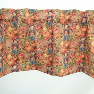 May include: A valance with a fall harvest pattern. The fabric features pumpkins, scarecrows, sunflowers, and baskets of apples in shades of orange, yellow, brown, and blue. The valance has a scalloped bottom edge.
