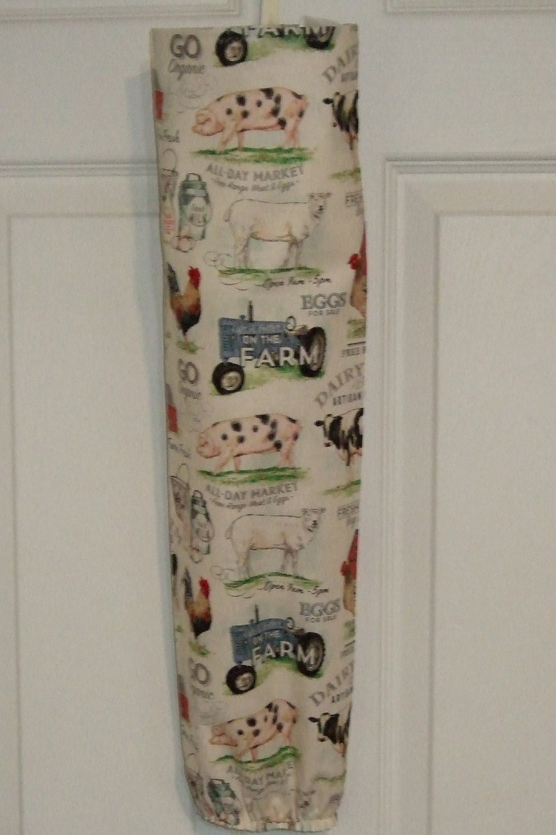 K&ouml;nnte beinhalten: Eine wei&szlig;e Stofftasche mit einem Bauernhof-Motiv. Die Tasche zeigt ein sich wiederholendes Muster aus Schweinen, Schafen, H&uuml;hnern, einem Traktor und den Worten "Go Organic", "All-Day Market", "Eggs for Sale", "On the Farm" und "Dairy Artisan".