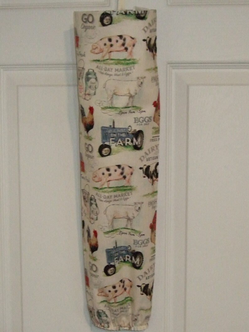 K&ouml;nnte beinhalten: Eine wei&szlig;e Stofftasche mit einem Farm-Motiv. Der Druck zeigt Schweine, K&uuml;he, H&uuml;hner, einen Traktor und den Text "Go Dairy", "All-Day Market", "Eggs for Sale" und "On the Farm".