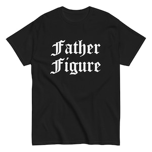 May include: Black t-shirt with the words "Father Figure" in a bold, white, gothic font. The text is centered on the front of the shirt. The shirt has short sleeves and a crew neck.