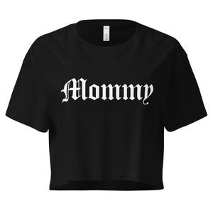 May include: Black crop top with the word "Mommy" in white gothic font. The shirt has short sleeves and a crew neck. The fabric appears to be a soft, lightweight material.