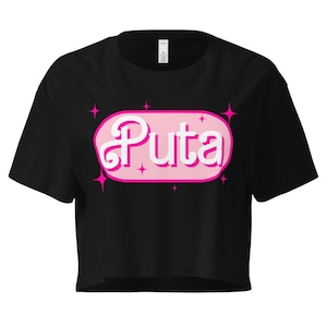 May include: Black crop top with the word "Puta" in white script inside a pink oval, surrounded by pink starbursts. The shirt is a casual style.