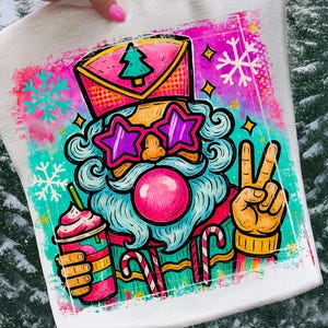 May include: A white t-shirt featuring a colorful graphic of Santa Claus wearing star-shaped sunglasses and a hat with a Christmas tree. Santa is holding a drink and giving a peace sign. The design includes snowflakes and candy canes.