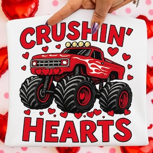 May include: White t-shirt featuring a red monster truck design with the words "CRUSHIN' HEARTS" in red. The truck has large black tires and is surrounded by red hearts. The design is perfect for Valentine's Day.