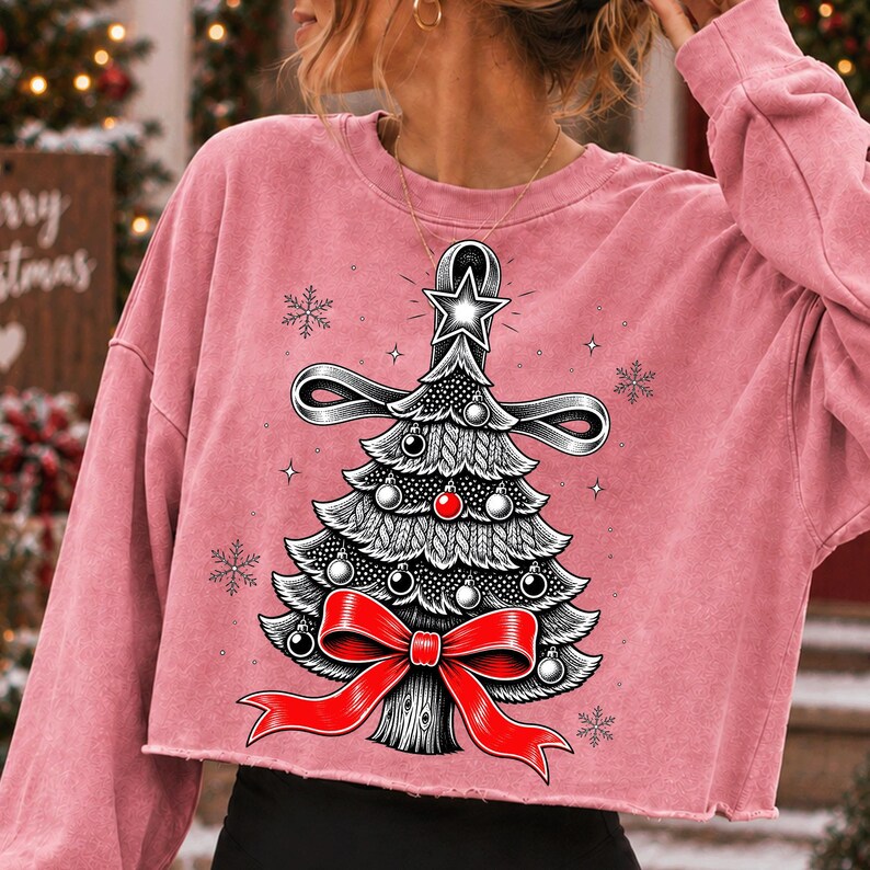K&ouml;nnte beinhalten: Ein altrosa lang&auml;rmeliges bauchfreies Sweatshirt mit einem Grafikdruck eines stilisierten Weihnachtsbaums. Der Baum ist in Schwarz-Wei&szlig; gehalten, mit einer leuchtend roten Schleife an der Basis, einer roten Kugel und einem wei&szlig;en Stern an der Spitze, umgeben von Schneeflocken.