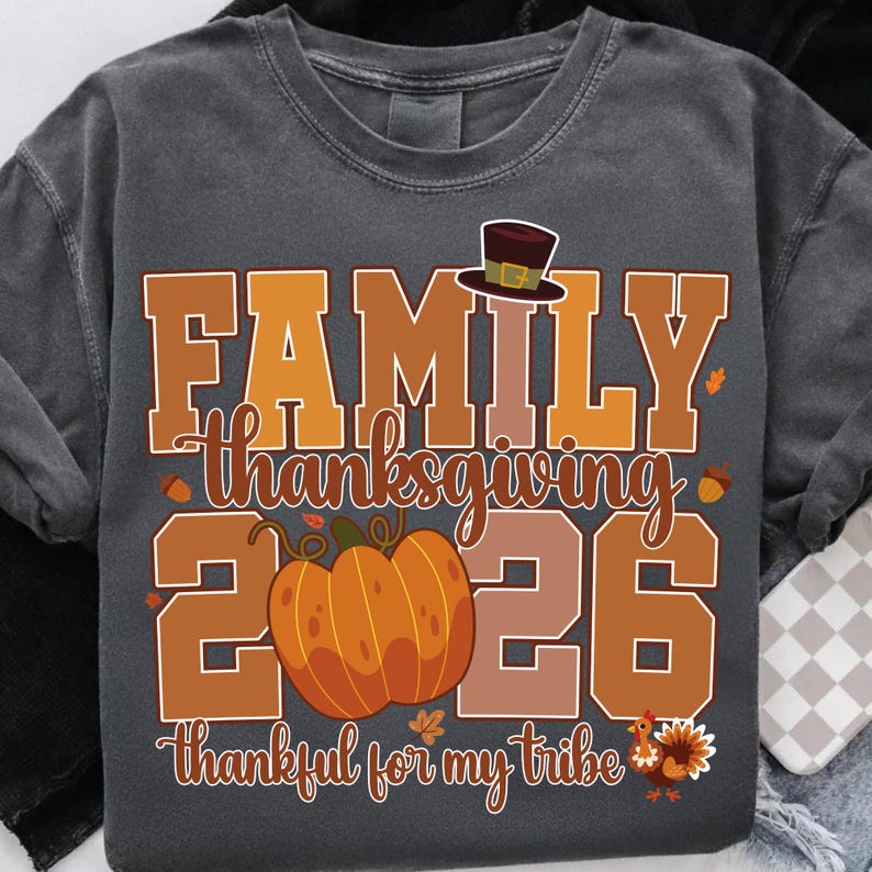 Pode incluir: Uma t-shirt cinzento-carv&atilde;o com um gr&aacute;fico que inclui o texto FAMILY THANKSGIVING 2026 e thankful for my tribe. O design apresenta um chap&eacute;u de peregrino castanho, uma ab&oacute;bora laranja, bolotas, folhas de outono e uma ilustra&ccedil;&atilde;o de um peru.