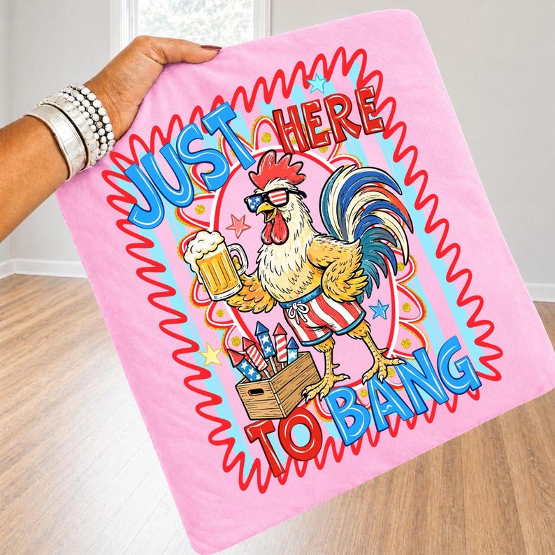 May include: Pink blanket with a cartoon rooster wearing sunglasses and patriotic shorts, holding a beer mug. The blanket has the text "JUST HERE TO BANG" in a wavy design. The rooster is standing next to a wooden crate of fireworks.
