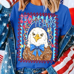 Pu&ograve; includere: Maglietta blu con un design patriottico. Presenta un'aquila con un papillon blu e la scritta "250 YEARS" in una cornice rossa e blu ornata di stelle.