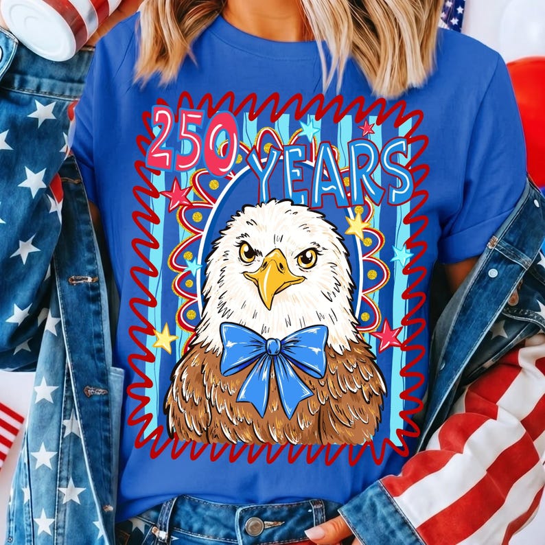 Pu&ograve; includere: Maglietta blu con un design patriottico. Presenta un'aquila con un papillon blu e la scritta "250 YEARS" in una cornice rossa e blu ornata di stelle.