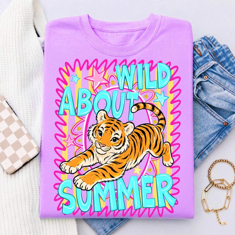 K&ouml;nnte beinhalten: Ein lilafarbenes T-Shirt mit einem Zeichentricktiger mit orangefarbenen und schwarzen Streifen. Der Text "WILD ABOUT SUMMER" ist t&uuml;rkis, mit einem rosa und gelben Hintergrund. Das Shirt ist mit Sternen und Wellenlinien verziert.