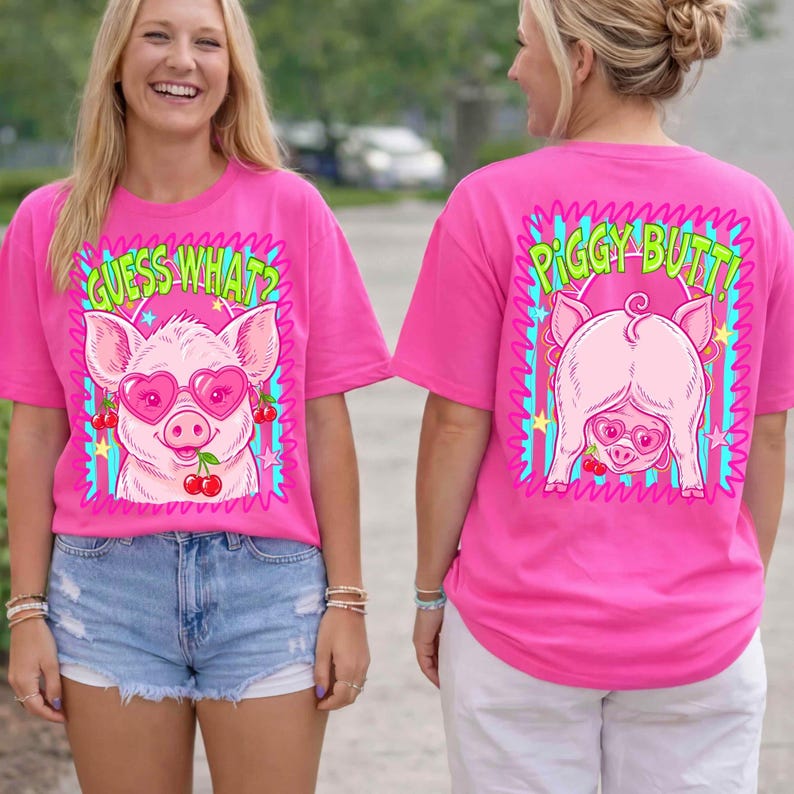 Op de afbeelding: Een felroze t-shirt met een cartoonvarken met een hartvormige zonnebril en kersen. De voorkant zegt "GUESS WHAT?" boven het varken. De achterkant van het shirt heeft een varkensachterwerk met de tekst "PIGGY BUTT!"