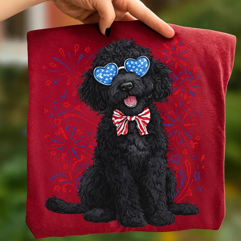 Pu&ograve; includere: Un asciugamano rosso con un cane nero che indossa occhiali da sole a forma di cuore con un motivo a stelle blu e un papillon rosso, bianco e blu. Lo sfondo presenta un disegno di fuochi d'artificio in rosso e blu.