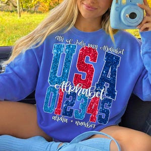 K&ouml;nnte beinhalten: Ein blaues Sweatshirt mit dem Text "4th of July png Alphabet" und "USA Alphabet 012345 alpha + number" in rotem und blauem Glitzer. Das Sweatshirt hat eine einfarbige blaue Farbe.