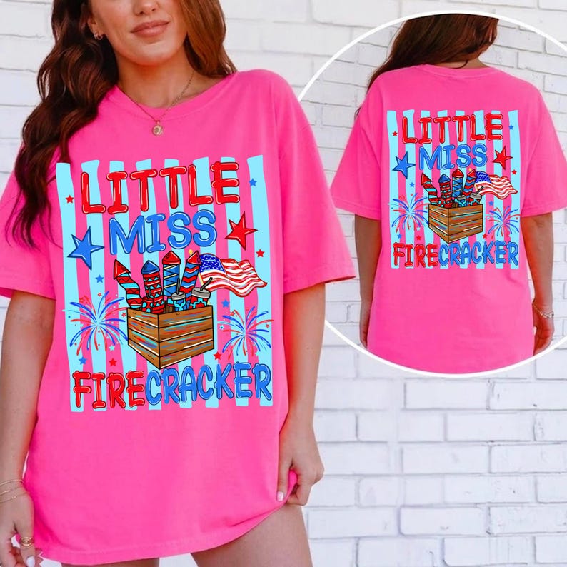 May include: A bright pink t-shirt with the text "Little Miss Firecracker" in red and blue. The design includes fireworks, stars, and an American flag. The back of the shirt also features the same design.