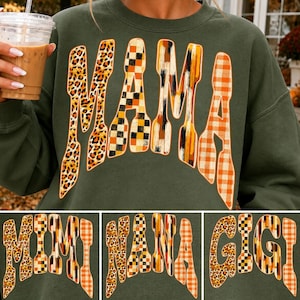 May include: An olive green crewneck sweatshirt featuring the word MAMA in large, stylized letters. Each letter has a unique pattern, including leopard print, black and white checkerboard, vertical brush strokes, and orange and white gingham.