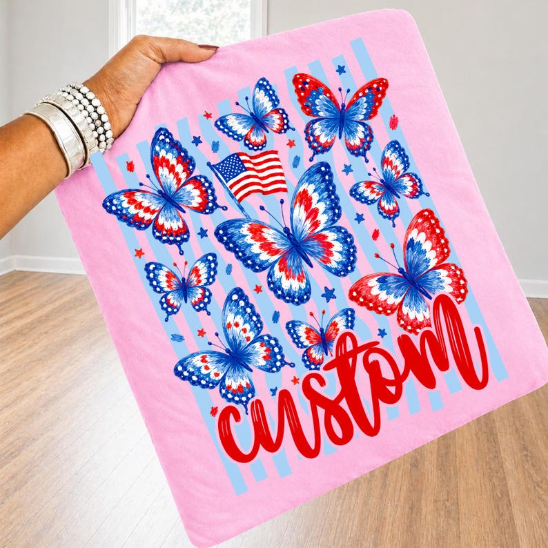 Peut inclure: Un carr&eacute; de tissu rose clair orn&eacute; de papillons aux ailes rouges, blanches et bleues. Le motif comprend un petit drapeau am&eacute;ricain, des &eacute;toiles bleues dispers&eacute;es et des rayures verticales bleu clair. Le mot custom est &eacute;crit en rouge.