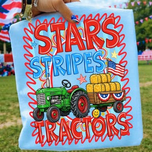 Pode incluir: Camiseta azul claro com as palavras "STARS STRIPES TRACTORS" em vermelho e azul. O gr&aacute;fico apresenta um trator verde puxando uma carro&ccedil;a com fardos de feno e uma bandeira americana. Uma estrela e um smiley tamb&eacute;m est&atilde;o inclu&iacute;dos.