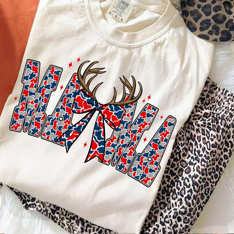 Pu&ograve; includere: T-shirt color crema con la scritta "MAMA" in un motivo mimetico rosso, bianco e blu. La lettera "A" &egrave; adornata da corna marroni e un fiocco. La maglietta &egrave; abbinata a pantaloni con stampa leopardata.