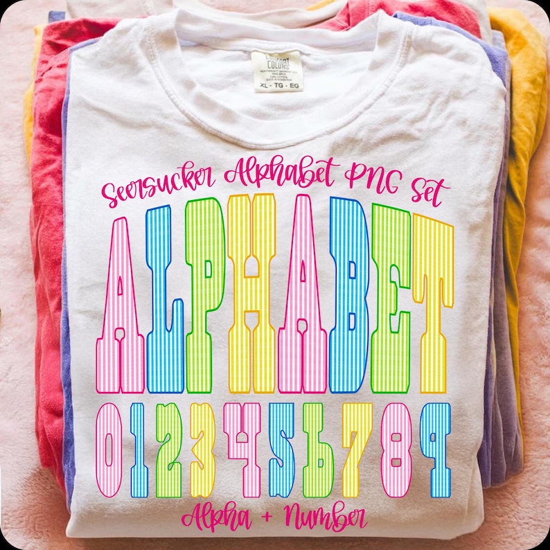May include: A white t-shirt featuring the text "Seersucker Alphabet PNG Set" in pink script. The word "ALPHABET" is in large, colourful, striped letters, with the numbers 0-9 below. The phrase "Alpha + Number" is at the bottom.