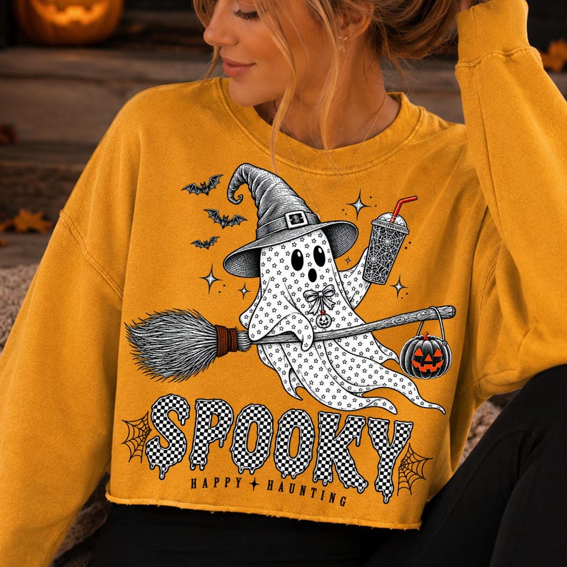 May include: A mustard yellow cropped sweatshirt featuring a graphic of a ghost wearing a witch hat, holding a drink and a broomstick with a jack-o'-lantern. The text reads "SPOOKY" in a black and white checkered pattern and "HAPPY HAUNTING" below.