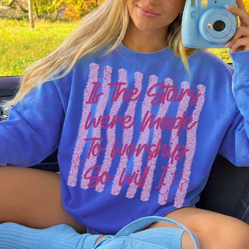 May include: A blue sweatshirt with the text "If The Stars Were Made To Worship So Will I" in pink. The text is arranged vertically with a striped background. The sweatshirt is a solid blue color.