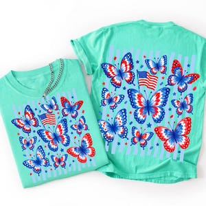 Puede incluir: Una camiseta de color verde menta con un patr&oacute;n repetitivo de mariposas con alas rojas, blancas y azules. El dise&ntilde;o incluye peque&ntilde;as banderas estadounidenses y estrellas dispersas. Las mariposas est&aacute;n dispuestas por la tela.