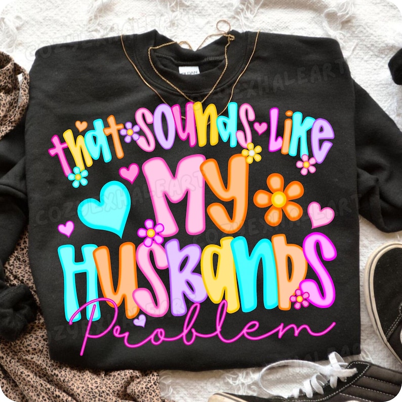 K&ouml;nnte beinhalten: Schwarzes Sweatshirt mit dem Schriftzug "that sounds like my husbands problem" in bunten Buchstaben. Das Design beinhaltet Blumen und Herzen in verschiedenen Farben. Eine goldene Halskette ist oben zu sehen.