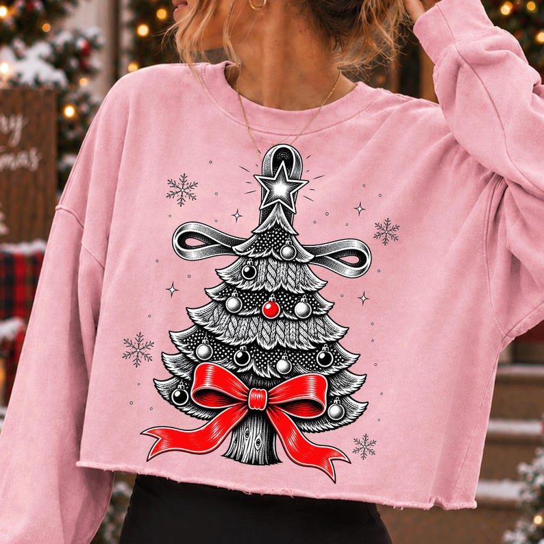 K&ouml;nnte beinhalten: Ein hellrosa, lang&auml;rmeliges bauchfreies Sweatshirt mit einer grafischen Illustration eines stilisierten Weihnachtsbaums. Der Baum ist mit schwarz-wei&szlig;en Ornamenten, einer leuchtend roten Schleife an der Basis und einem Stern an der Spitze verziert.