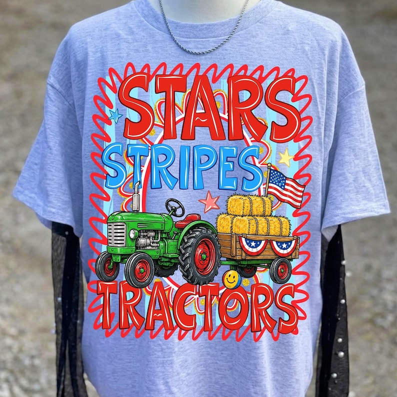 Pode incluir: Camiseta azul clara com um gr&aacute;fico de um trator verde puxando uma carro&ccedil;a de fardos de feno e uma bandeira americana. O texto "STARS STRIPES TRACTORS" est&aacute; em vermelho e azul.