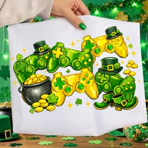 May include: White St. Patrick's Day themed graphic featuring green and yellow video game controllers, a pot of gold, and leprechaun hats and boots. The design includes shamrocks and gold coins, with star accents.