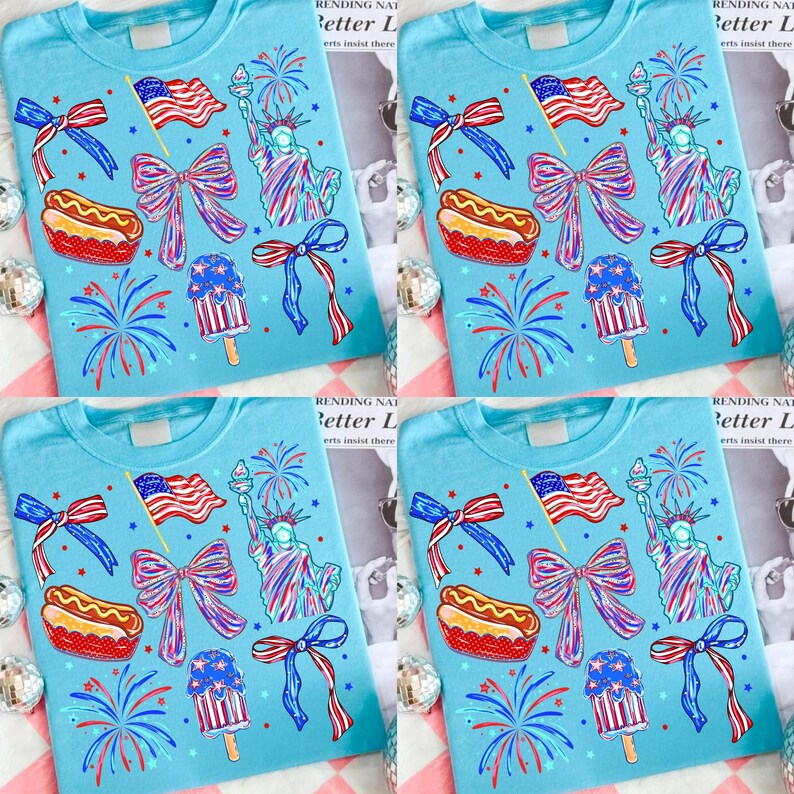 K&ouml;nnte beinhalten: Hellblaues T-Shirt mit patriotischen Grafiken. Das Design umfasst eine amerikanische Flagge, die Freiheitsstatue, Feuerwerk, Schleifen, einen Hotdog und ein Eis am Stiel. Das Shirt hat einen Rundhalsausschnitt.