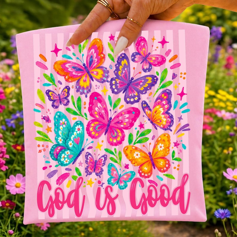 May include: A light pink rectangular fabric item featuring a vertical striped pattern and a colorful print of various butterflies in shades of pink, purple, blue, orange, and yellow, with the text God is Good written in a pink cursive script.