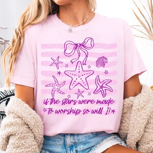 Op de afbeelding: Lichtroze T-shirt met paarse zeesterren, een strik en een schelp. De tekst "if the stars were made To worship so will I!" staat eronder. Het shirt heeft korte mouwen.