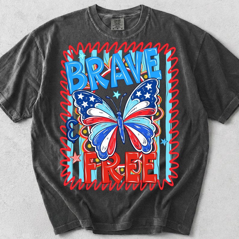 May include: Dark grey t-shirt with a patriotic butterfly design. The butterfly has red, white, and blue wings with stars. The words "BRAVE & FREE" are in blue and red, with a red zigzag border.