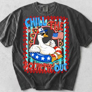 Peut inclure: T-shirt gris fonc&eacute; avec un dessin d'oie de dessin anim&eacute; portant des lunettes de soleil et un chapeau patriotique, tenant un petit drapeau am&eacute;ricain. Le t-shirt porte les mots "Chill the Fourth Out" en rouge et bleu, avec un design festif.
