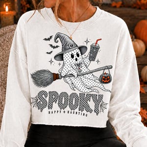 May include: A white long-sleeve sweatshirt featuring a graphic of a ghost wearing a witch hat, riding a broomstick, and holding a drink. The ghost wears a bow tie and carries a jack-o'-lantern. The text reads SPOOKY HAPPY HAUNTING.